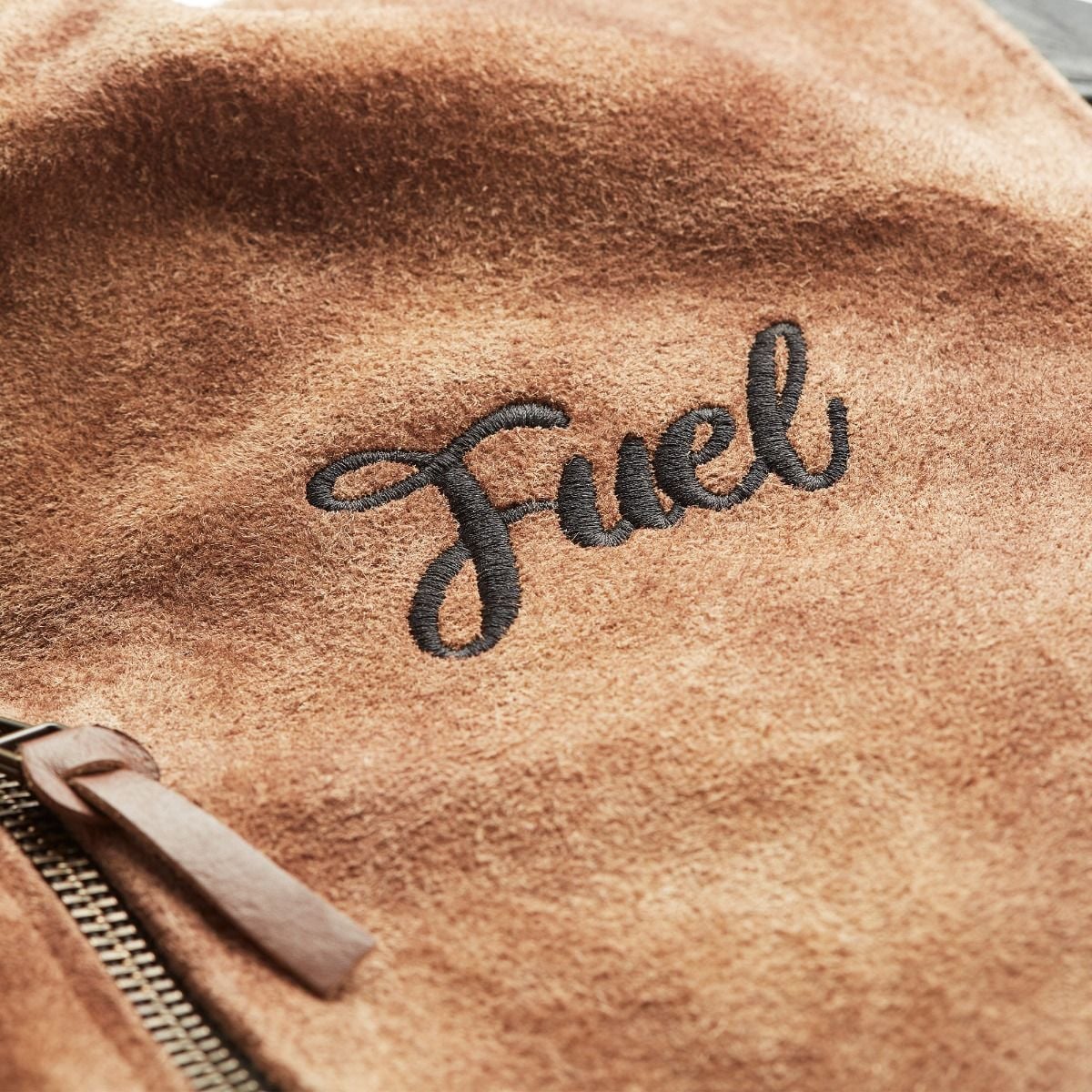 Close-up of black Fuel embroidery on the tan suede jacket